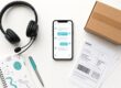 KI Kundenservice: Smartphone mit Chat-Oberfläche, Headset, Versandetiketten und Paket als Flatlay – Fokus auf